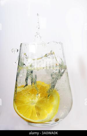 a slice of lemon falls into a glass of soda, with water splashes fly out of the glass homemade lemonade Stock Photo