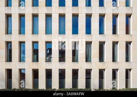 A contemporary building exterior featuring a beige stone facade with a repetitive pattern of narrow, rectangular windows. Stock Photo