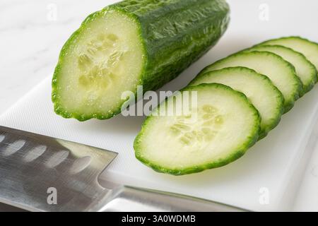 Cut in half cucumber, juicy slices and kitchen knife close-up. Cooking vegetarian salad of fresh green cucumbers. Organic vegetables, healthy eating. Stock Photo