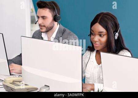 Focused call center operators with headsets working in front of computer monitors at open space office Stock Photo