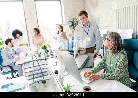 Busy working office with professionals collaborating on tasks during daylight hours, multi-age Stock Photo