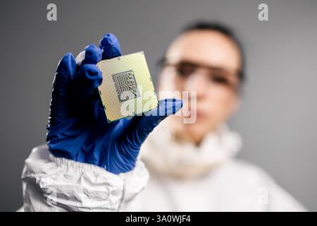 In a high-tech electronics factory, a design engineer in a sterile coverall examines a microchip with gloves, perfect for showcasing innovation Stock Photo