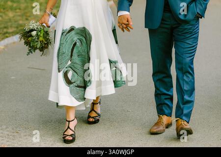 Couple walks hand in hand on a park path, dressed in formal attire, enjoying a romantic moment together. Stock Photo