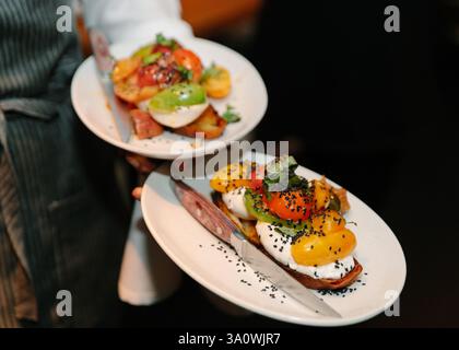 Two beautifully plated dishes featuring vibrant vegetables and creamy toppings are served at a lively urban restaurant. Stock Photo