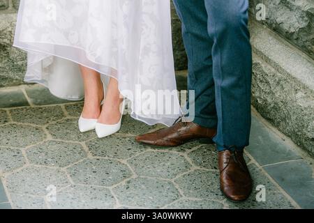 Bride and groom stand together, their elegant footwear showcased on a patterned stone in a serene outdoor setting. Stock Photo