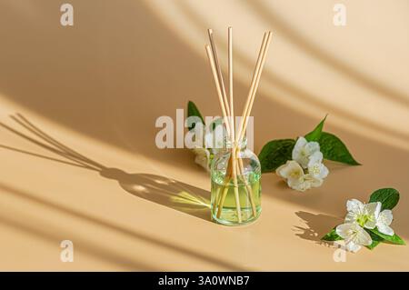 An aesthetically pleasing setup featuring a glass bottle filled with light green essential oil, diffusing wooden sticks, delicate white flowers. Stock Photo