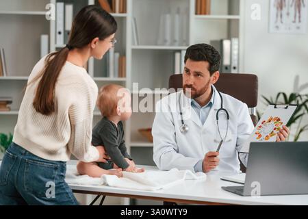 Having consultation. With baby and mother. Doctor in formal clothes is working in the cabinet. Stock Photo