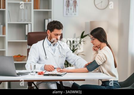 Measuring blood pressure. With woman. Doctor in formal clothes is working in the cabinet. Stock Photo