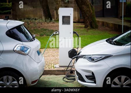 An electric vehicle at a charging station in the city. White e-car that is on the charging cable. The electric car is shown from the side where the en Stock Photo