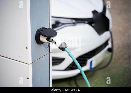 An electric vehicle at a charging station in the city. White e-car that is on the charging cable. The electric car is shown from the side where the en Stock Photo