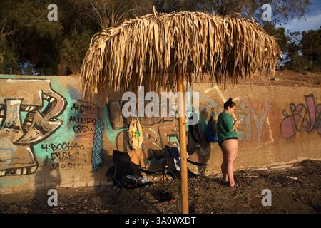 Woman using Mobile Phone Standing by Wall with Graffiti at Vouliagmeni Beach Attica Greece Stock Photo