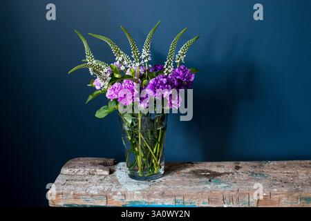Wedding bouquet of Veronica and Moondust carnations in a glass vase on a rough wooden vintage bench against a dark blue background. Space for text. Stock Photo