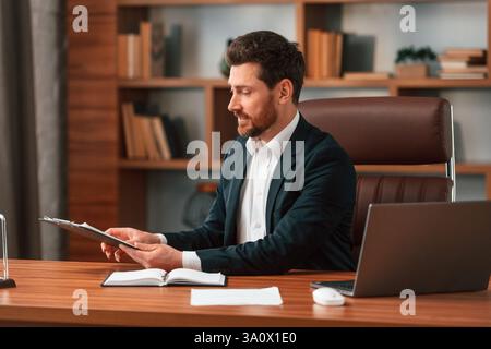 Working with documents. Businessman in formal clothes is indoors. Stock Photo
