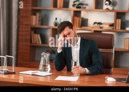 Having headache, feeling bad. Businessman in formal clothes is working indoors. Stock Photo