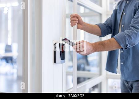 Man uses his smartphone to access a secure area, highlighting modern security technology and mobile access solutions. Stock Photo