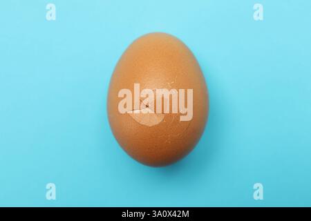 One egg with cracked shell on light blue background, top view Stock Photo