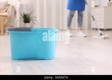 Woman cleaning floor with string mop indoors, focus on bucket Stock Photo