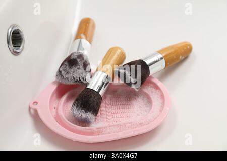 Makeup brushes with soap and cleansing pad in sink, closeup Stock Photo