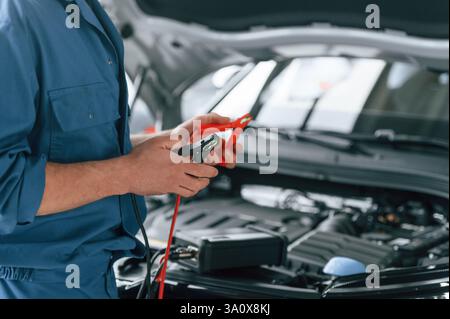 Testing breakage by using electrical terminals. Man in blue uniform is working in the car service. Stock Photo