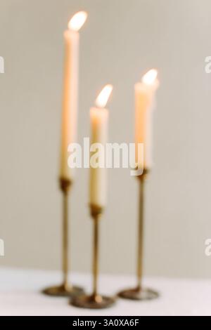 Three tall candles flicker gently in brass holders, creating a warm and relaxing ambiance in a peaceful environment. Stock Photo
