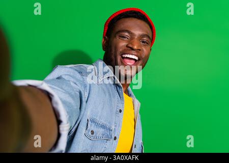 Smiling young man in a vibrant casual outfit taking a self-portrait against a green background exuding happiness Stock Photo