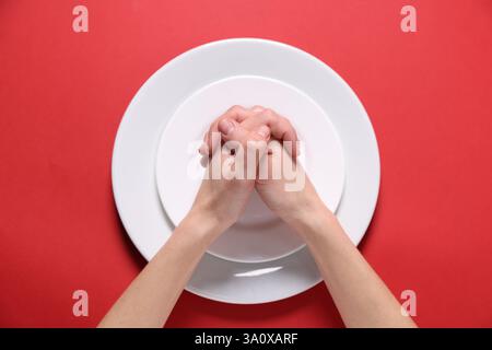 Woman holding hands together over plates on red background, top view Stock Photo