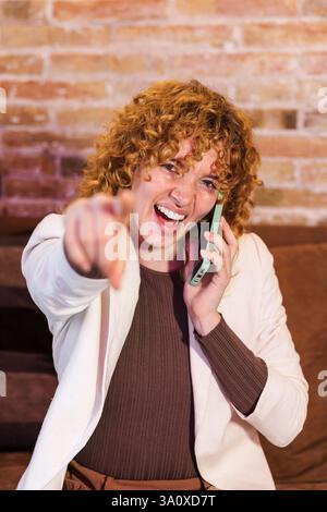 Enthusiastic freelancer pointing finger while talking on phone Stock Photo