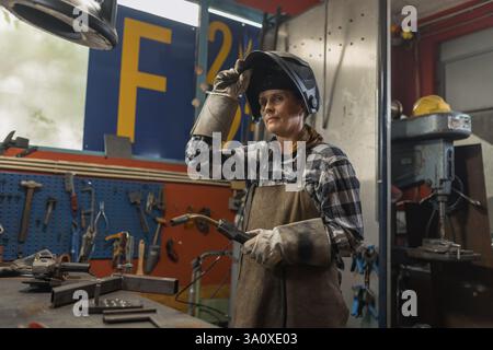 Woman in protective equipment uses tools and machines in welding metal workshop. Stock Photo