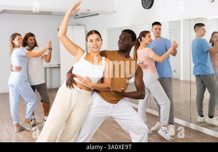 Joyful young adult couples learning passionate pair dancing during practicing in choreography class Stock Photo