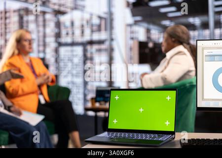 Multicultural team of specialists using mockup copy space in the office, working with resilience to accomplish enterprise objectives. Manager and employees meeting for a briefing. Stock Photo