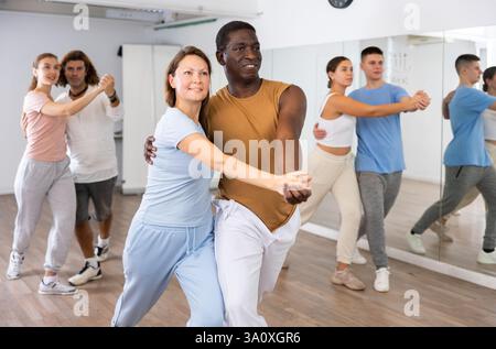 Smiling dancing people practicing movements while dancing in pairs in dance school for adults Stock Photo
