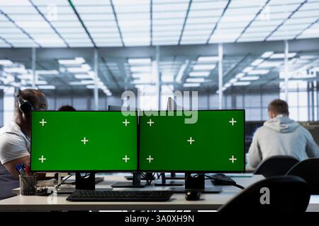 Technicians in data center using green screen PCs to coordinate deployment of server architecture. Server hub workers configuring and testing equipment with chroma key computers Stock Photo