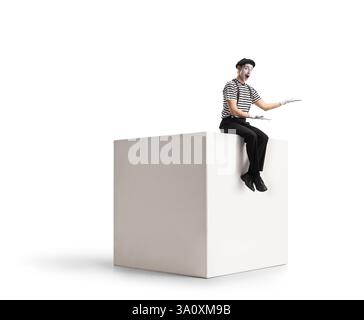 Mime sitting on a white cube and gesturing with hands isolated on white background Stock Photo