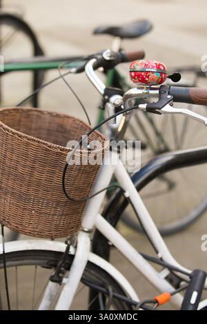 White bicycle with wicker basket parked on city street, likely near a landmark.  Basil bell. Stock Photo