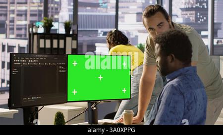 Admin doing software debugging on green screen PC, asking for help from coworker, checking errors in code. Worker fixing coding mistakes on mockup computer, being assisted by colleague, camera A Stock Photo