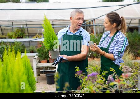 Positive man and woman in uniform taking photo of name of plant on smartphone in conservatory Stock Photo