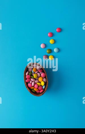 Chocolate Easter egg with colorful dragees inside on a blue. Happy Easter. Stock Photo