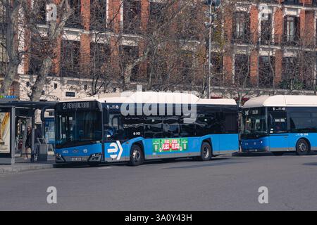Madrid, Spain. February 15, 2025. A blue EMT Madrid bus at a city bus stop and historic buildings in the background Stock Photo