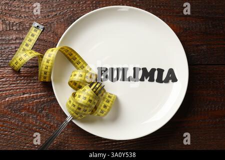 Plate with word Bulimia, fork and measuring tape on wooden table, top view Stock Photo