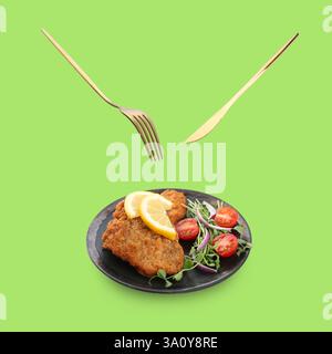 Cutlery in air over plate with delicious schnitzels on light green background Stock Photo