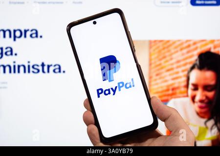 BOGOTA, COLOMBIA - MARCH 05 OF 2025 A male hand holding a smartphone with paypal global payment service logo and blurred paypal interface at backgroun Stock Photo