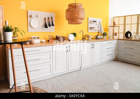 Interior of stylish kitchen with white counters and hanging peg boards on yellow wall Stock Photo