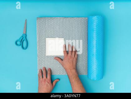 photo mockup template being packaged with bubble wrap scissors male hands Stock Photo