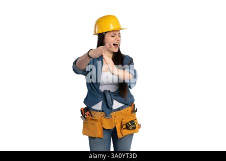 A construction worker woman in a yellow hard hat and denim shirt is using her hands to show a stop gesture, symbolizing the importance of safety and c Stock Photo