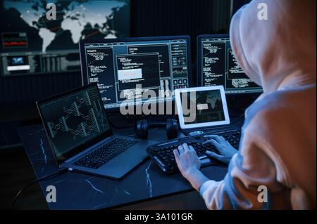 View from behind. Young professional female hacker is indoors by computer with lot of information on displays. Stock Photo