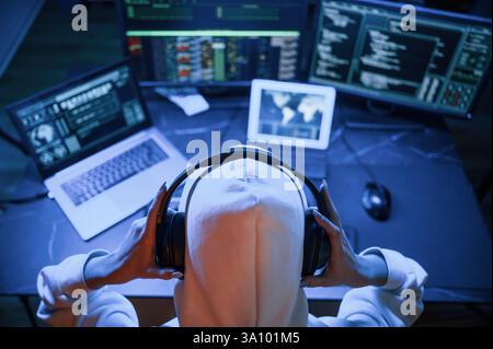 Blue neon light. Young professional female hacker is indoors by computer with lot of information on displays. Stock Photo