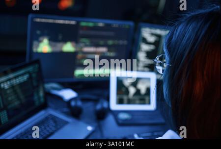 Young professional female hacker is indoors by computer with lot of information on displays. Stock Photo