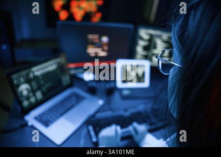 Young professional female hacker is indoors by computer with lot of information on displays. Stock Photo
