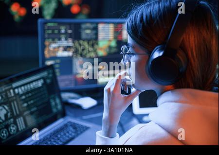 Focused on work. Young professional female hacker is indoors by computer with lot of information on displays. Stock Photo