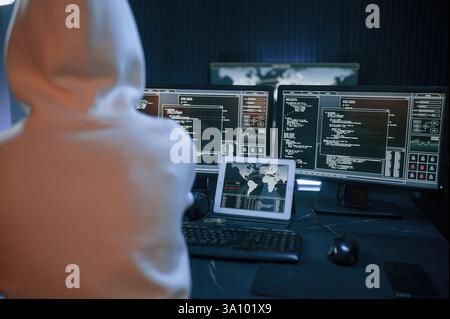 Young professional female hacker is indoors by computer with lot of information on displays. Stock Photo